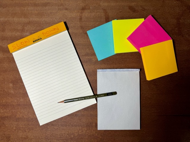 A photo of the Rhodia, some very bright Post-its, and the (grey kinda boring) cheap Muji pad on my desk.